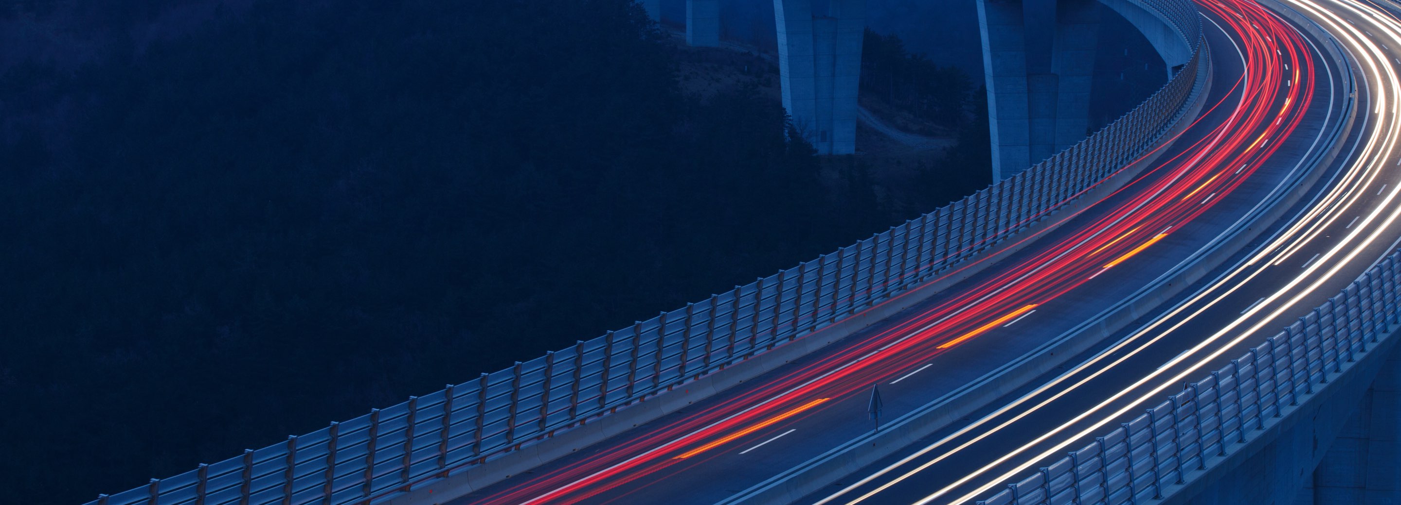 A highway overpass at night with the lights of cars blurred from moving quickly.