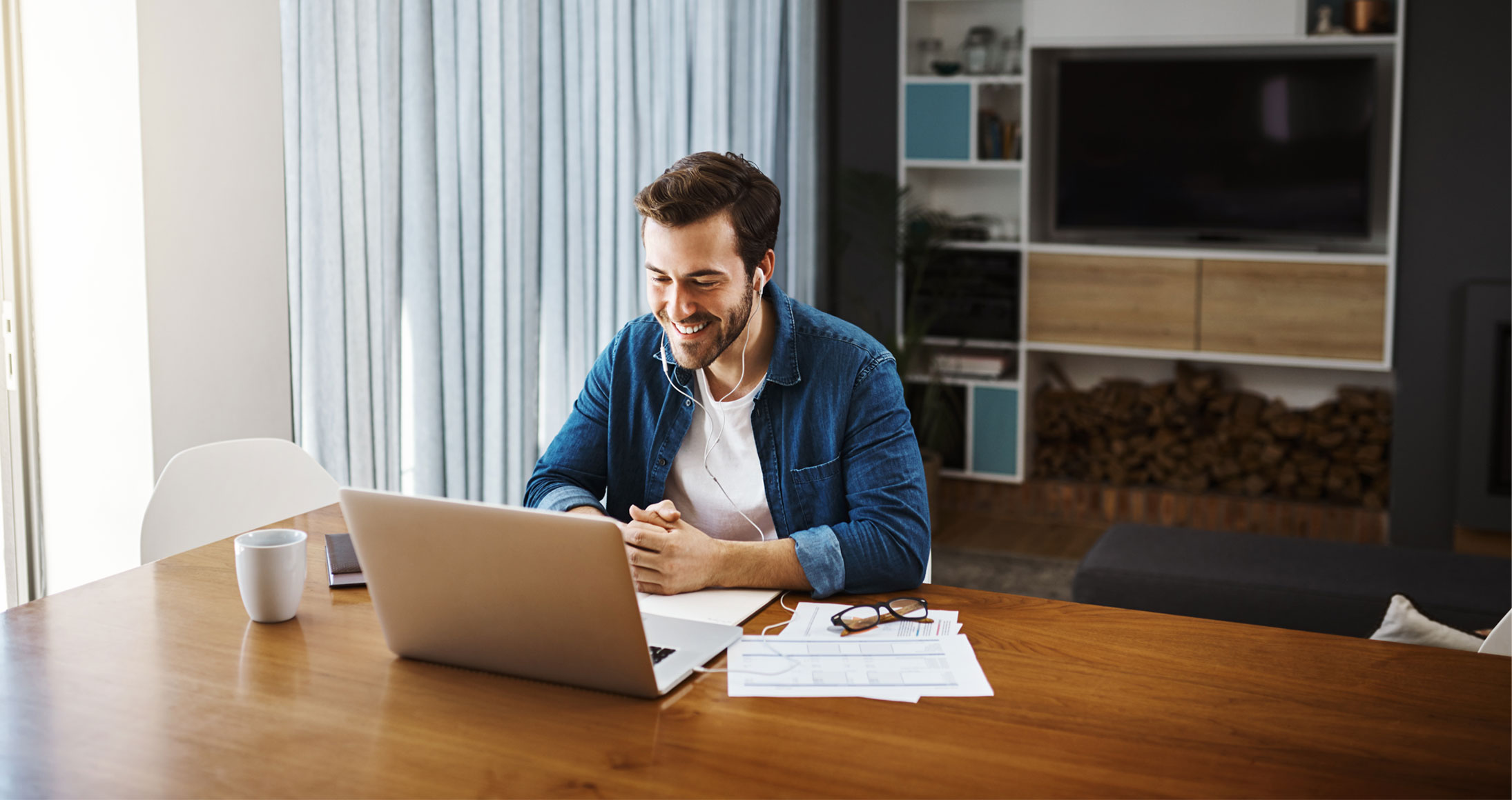 A man sitting at a table in front of a laptop while wearing headphones.