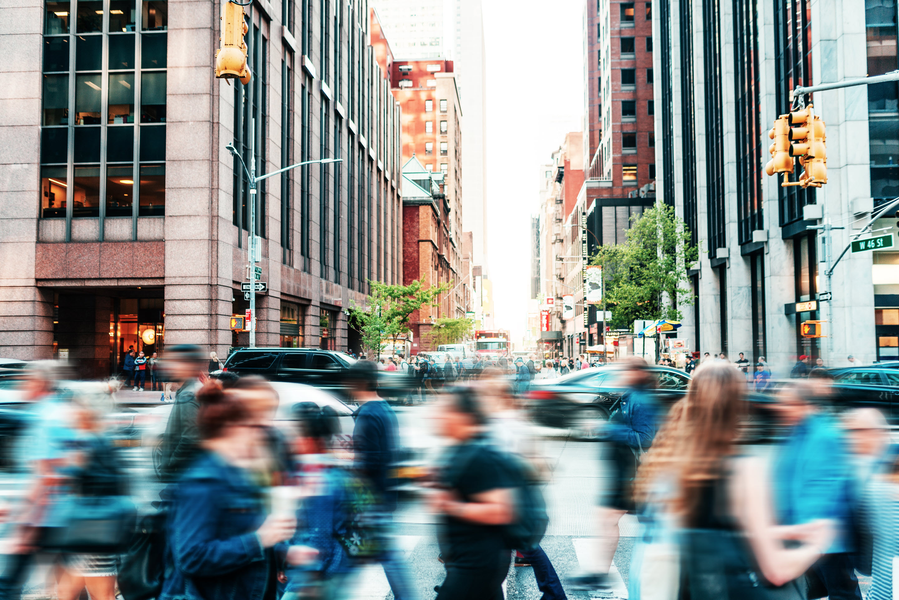 A busy city street, filled with a blur of people crossing at the crosswalk.