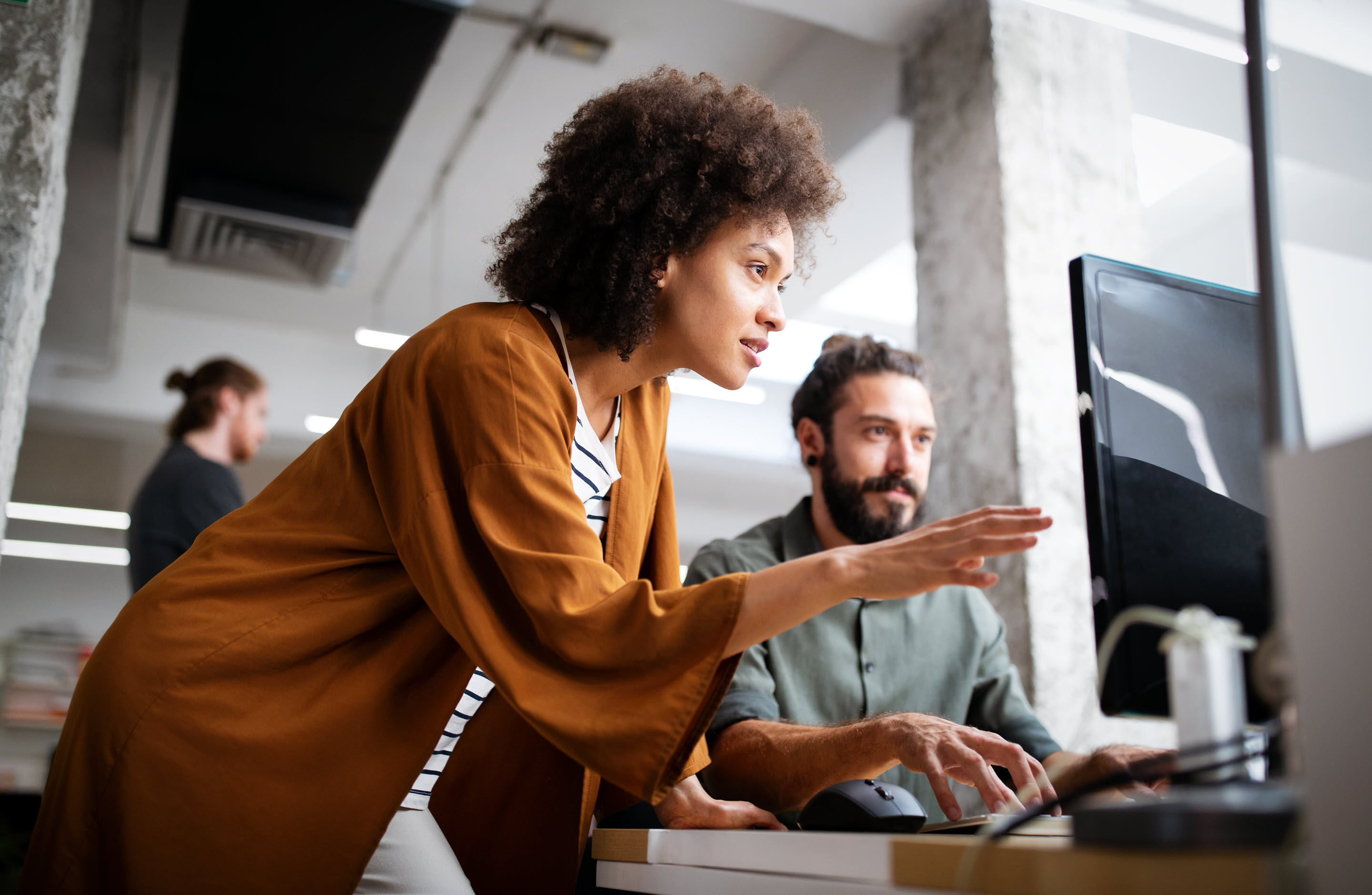 A businesswoman points at an item on an IT professional's screen, suggesting how to optimize his tax technology.