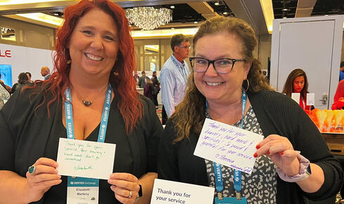 Two customers at Vertex Exchange, holding up notecards thanking members of the US military for their service.