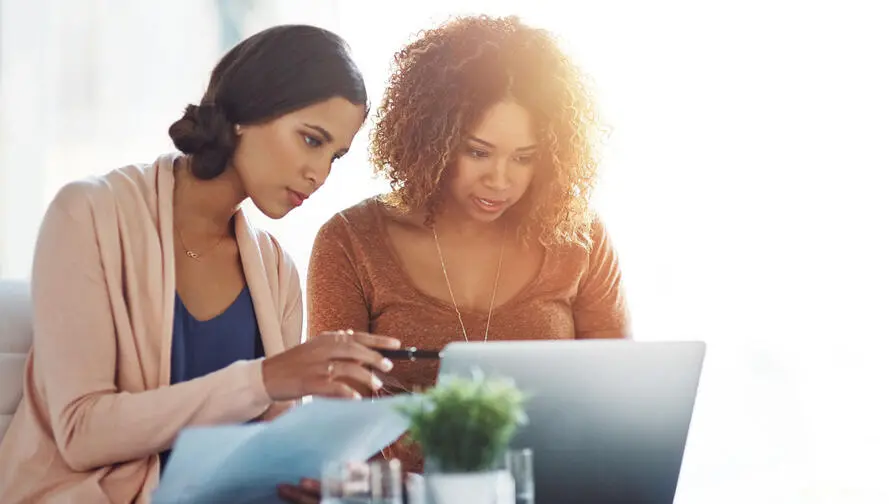 Two women reviewing tax data on laptop.