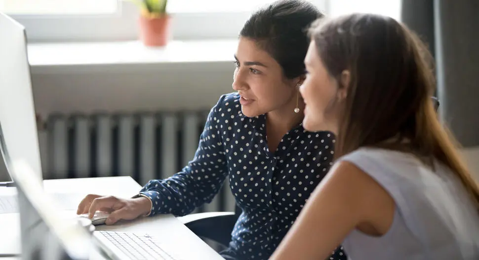 Two women lean towards a computer monitor to examine their continuous compliance processes as it relates to digital invoices.